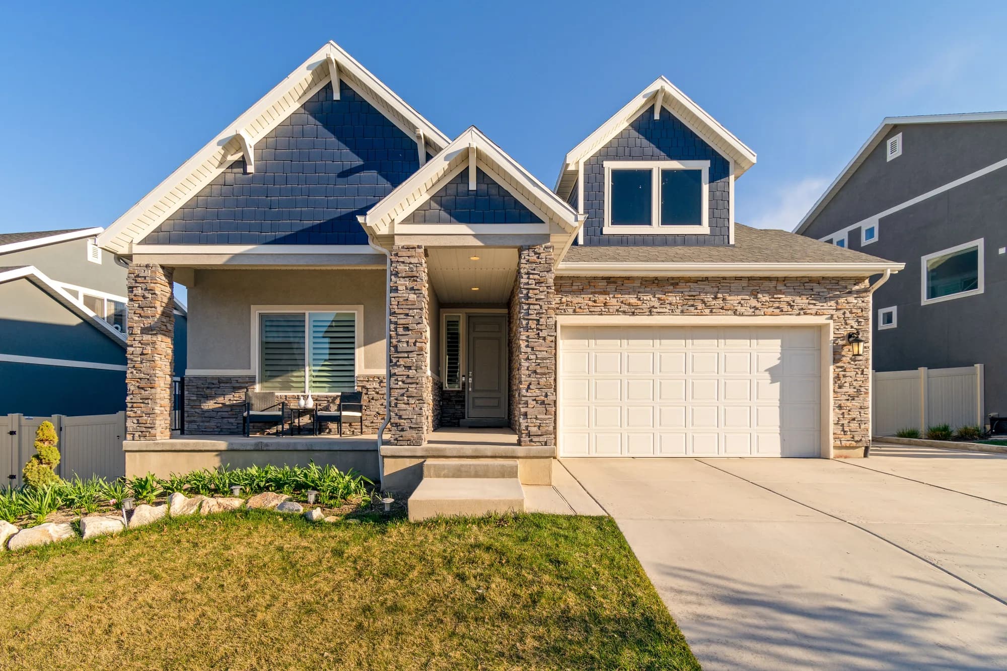 A blue craftsman-style home with stone columns and a two-car garage